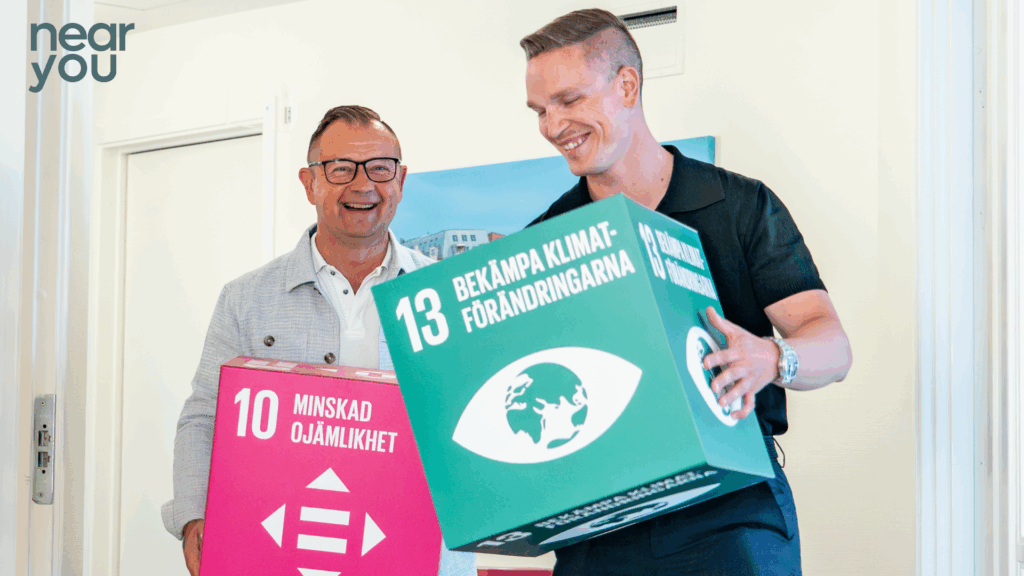 Två leende män håller i boxar med globala mål