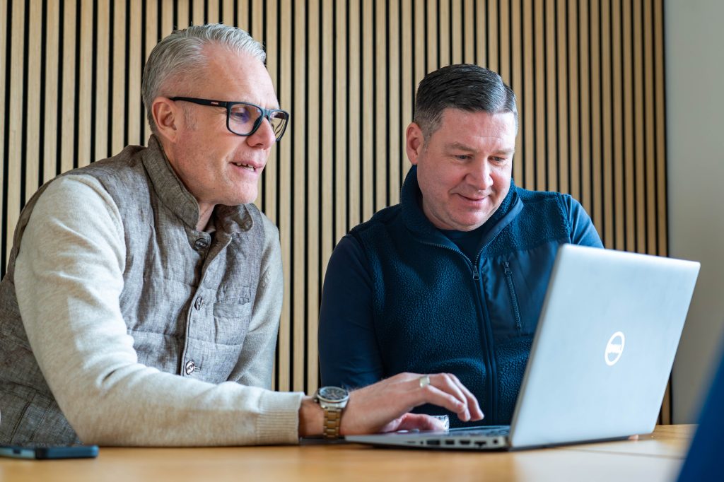 Två leende män sitter vid en dator